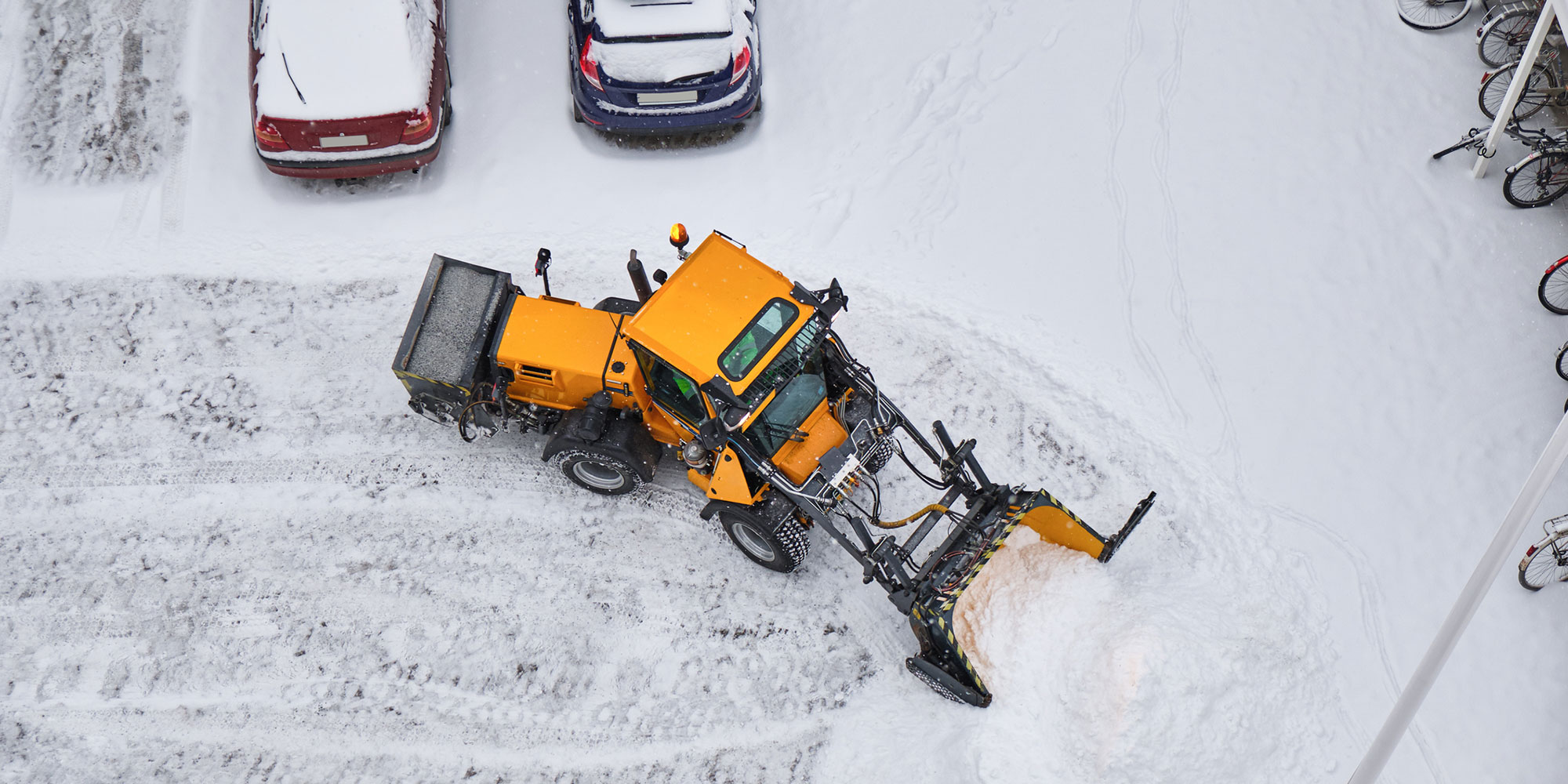 Gul traktor som snöröjer på parkering